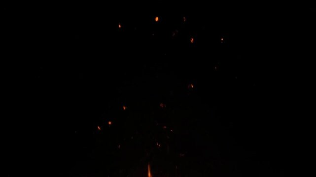 Dramatic rising fire sparks. Bright orange embers floating against a dark night sky, ideal for cinematic overlays and visual effects.