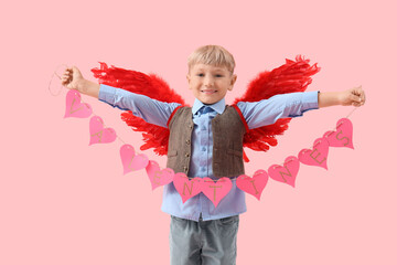Obraz premium Cute little happy boy in cupid wings with heart-shaped garland on pink background. Valentine's Day celebration