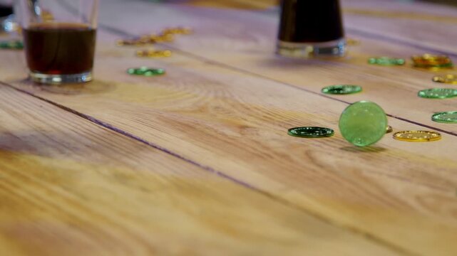 Man spinning a dreidel, green and gold gelt scattered on a wooden table, with drinks in background