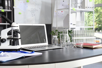 Laptop with microscope and glassware on table in laboratory