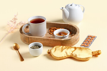 Fototapeta premium Sleep mask, pills and tea set with wooden tray on beige background