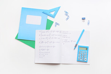 Fototapeta premium Open copybook with math formulas and stationery on light background