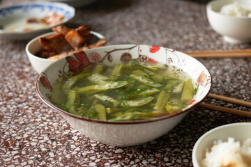 A bowl of fresh sliced okra soup in clear broth, a popular and healthy rustic dish in a traditional Vietnamese family meal setting
