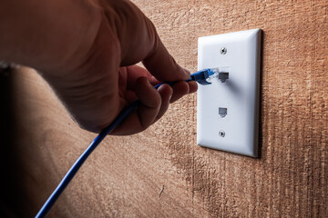 A close-up, high-detail shot of a hand plugging a blue RJ45 Ethernet cable into a white...