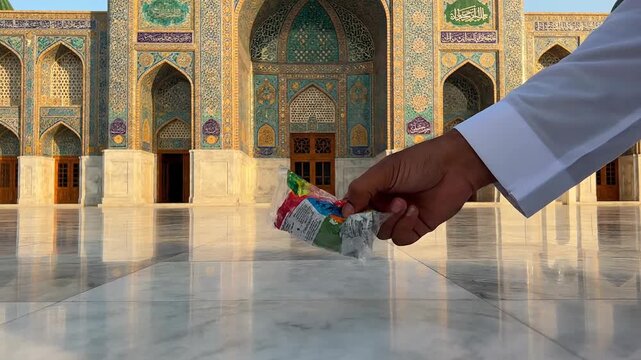 Hand picking up colorful candy wrapper from marble floor in front of ornate mosque