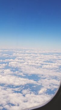 Aerial view from an airplane window above white puffy clouds and a clear blue sky creating a serene travel scene. High quality 4k footage