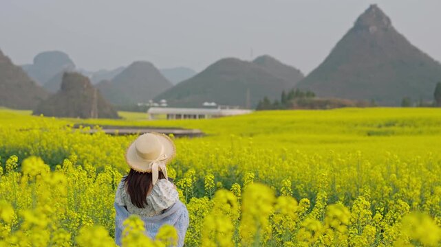 Young woman tourist enjoying and taking a photo the beautiful canola fields while traveling in Luoping, China