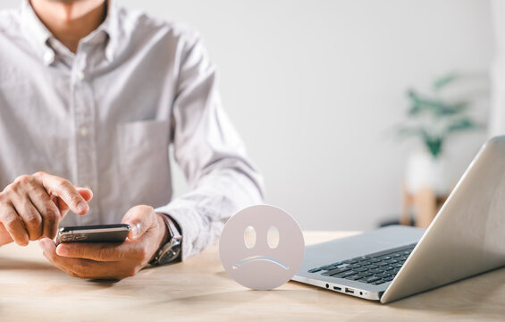 Customer negative feedback, expressing unhappiness with service, leaving bad review using mobile phone, showing dissatisfaction with online experience, poor satisfaction rate shown by sad face icon