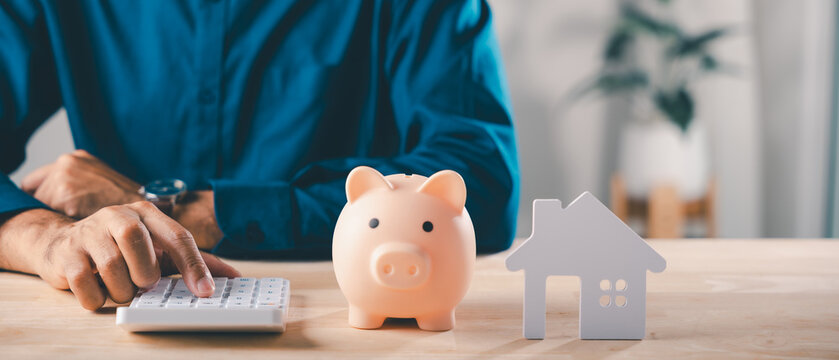 Real estate money investment, piggy bank home saving, man uses calculator near small house model while planning finance to save, buying property through bank, mortgage insurance