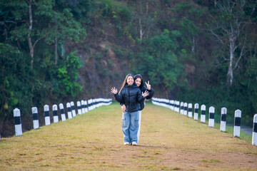 Asian people family by mother and daughter taking photo together and embrace hug of love to stick out tongue two fingers up gesture on valentine day at dam embankment in Pang Ung Reservoir Thailand