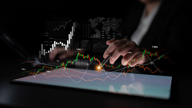 A business professional reviews financial data on a tablet with stock market graphs and charts, highlighting trends and investment strategies in a modern workspace. Scalp