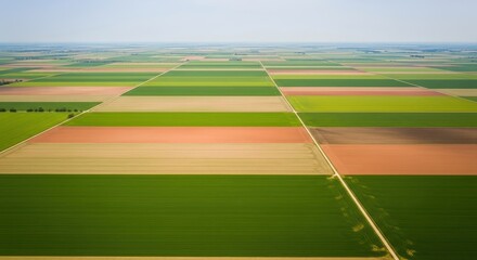 Obraz premium Expansive agricultural landscape viewed from above, showcasing diverse crop fields with vibrant color patterns and intersecting roads.