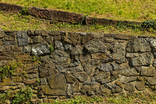 Old stone retaining wall in a public park with green grass and trees on a sunny day