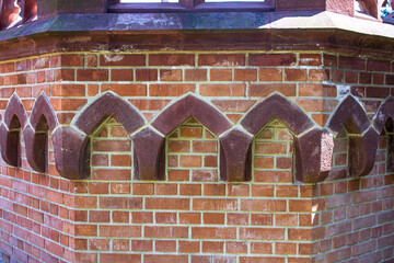 Close-up of a decorative red brick wall with gothic arched corbels on a historic castle tower © Janiel Kaffe