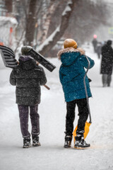 Teenagers carry snow shovels on a snowy sidewalk on a winter day