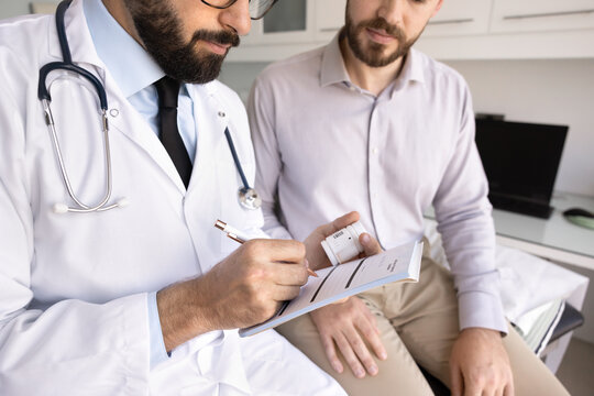Giving prescription note. Close up cropped shot doctor holding pen write paper medical receipt on pharmaceutical product for patient hold container with drugs. Prescribing treatment procedure concept