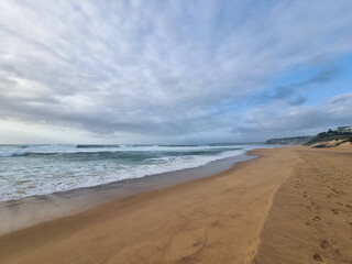 Fototapeta premium Waves on the sand at Bar Beach Newcastle New South Wales Australia early morning under a grey cloudy sky
