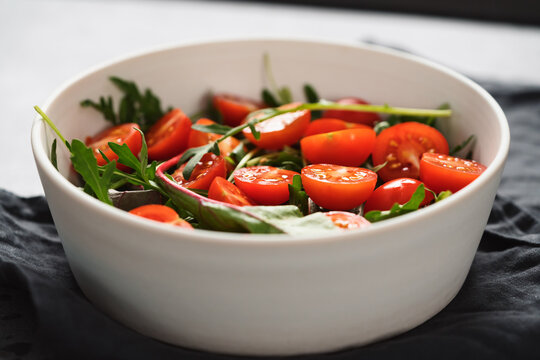 salad with cherry tomatoes and mixed grens in white bowl on concrete background
