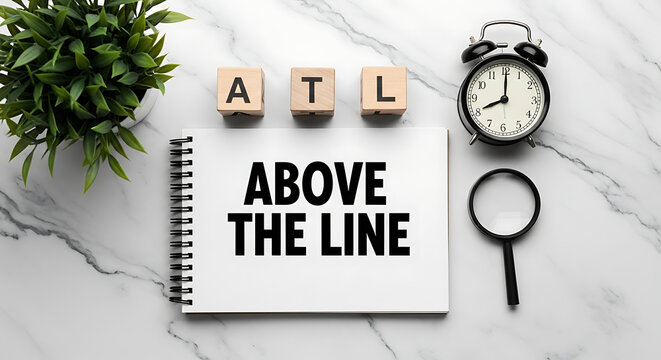 A top-down view of a notepad on a marble surface with the acronym "atl" and the phrase "above the line" written on it
