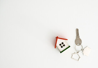 A model house and metal keys on a white background with a place for text, top view. Concept for buying or renting real estate