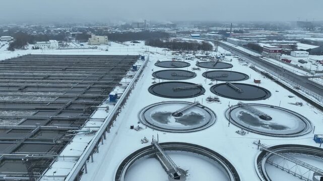 Snow-covered treatment plant features multiple round aeration and settling pools. Geometric rhythm dominates cold industrial landscape