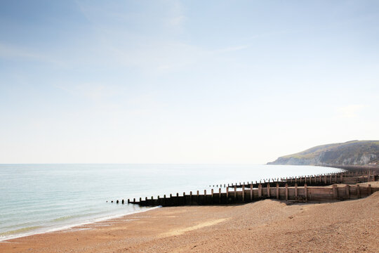 Tranquil Coastal Scene With Wooden Breakwater Along Quiet Beach and Distant Cliffs Under Clear Sky Evening