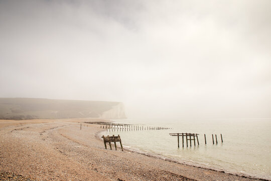 Mist Over a Quiet Seaside With Ruined Docks and Cliffs Along a Pebble Beach