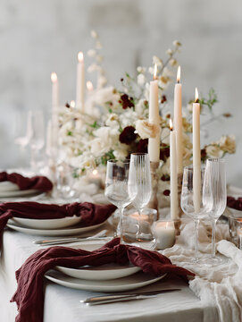 Elegant burgundy and cream wedding tablescape with candles, glassware and floral centerpiece creating romantic warm atmosphere