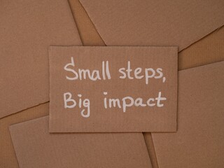 Cardboard with handwritten words Small Steps, Big Impact on a cardboard pieces background.