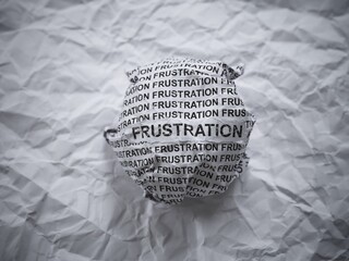 Crumpled paper ball with words Frustration on a crumpled white paper background.