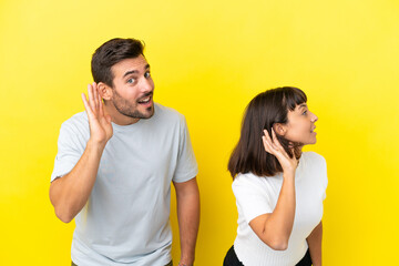 Fototapeta premium Young couple isolated on yellow background listening to something by putting hand on the ear