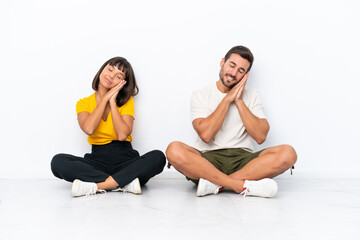 Obraz premium Young couple sitting on the floor isolated on white background making sleep gesture in dorable expression