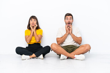 Fototapeta premium Young couple sitting on the floor isolated on white background surprised and shocked while looking right