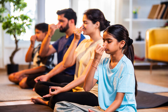 Happy Indian parents and kids practicing pranayama yoga together indoors for healthy lifestyle