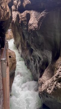 spring river flowing through the narrow rocky partnach gorge. water dripping from above creates a fairy tale atmosphere, with dramatic cliffs and a narrow rock path where tourists are walking.garmisch