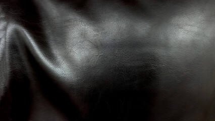 Fototapeta premium A close-up of draped black leather with fine grain texture. Soft highlights glint off the ripples and folds, creating sleek luxurious and moody aesthetic suitable for high-end backgrounds