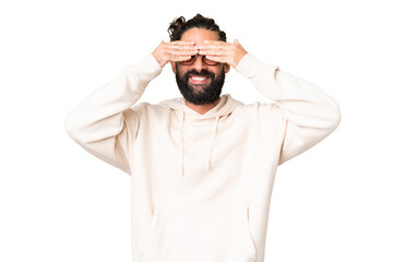 Fototapeta premium Young man with beard over isolated chroma key background covering eyes by hands and smiling