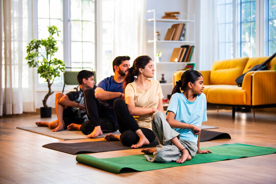 Indian parents and children performing seated spinal twist yoga together indoors