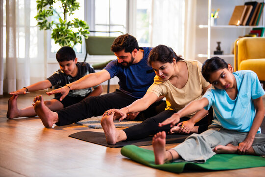 Indian parents and children performing seated head to knee yoga together indoors