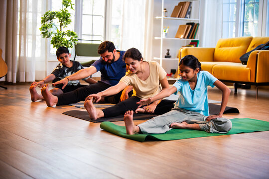 Indian parents and children performing seated head to knee yoga together indoors