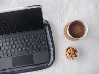 Digital tablet computer with hot cocoa and peanuts on white table, sense of working and relaxed.