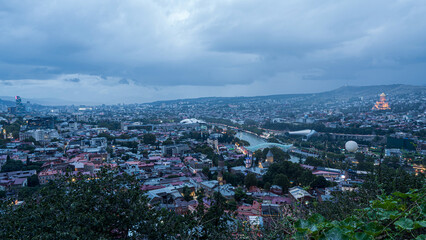 Evening cityscape of Tbilisi, Georgia, with cloudy sky and city lights reflecting on Kura River. © banphote