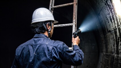 Engineer inspecting a dark underground tunnel with a flashlight