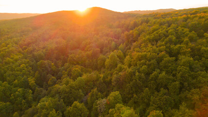 Obraz premium AERIAL: Morning sun rising behind gorgeous hilly countryside with lush forest
