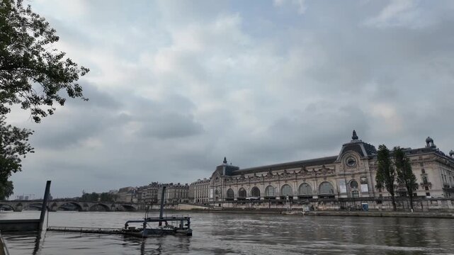 Navigating the seine river past the historic mus&eacute;e d'orsay in paris, france on a cloudy day, showing its impressive beaux-arts architecture and famous clock face