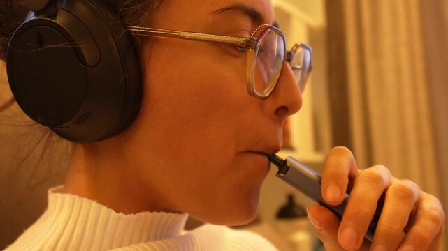 Focused woman wearing headphones vaping indoors