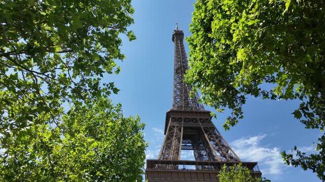 Majestic low-angle view of the eiffel tower in paris, france. The iconic landmark stands against a brilliant blue sky, beautifully framed by the lush green leaves of nearby trees