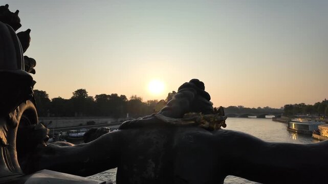 Scenic sunset over the seine river in paris from the pont alexandre iii, featuring a detailed silhouetted statue with golden elements and tour boats cruising along the water