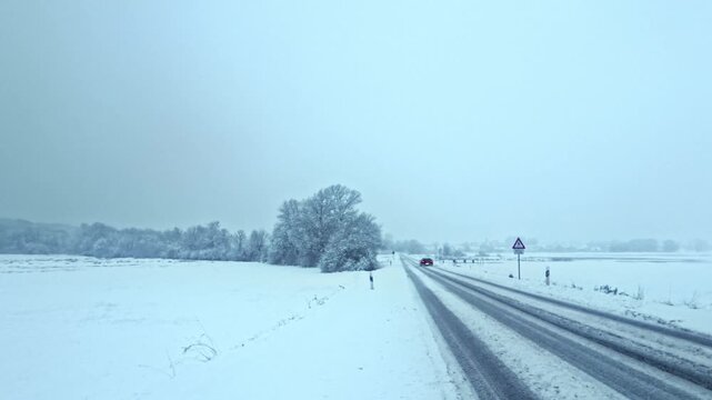 winterliche verschneite Landstra&szlig;e: Auto, Stra&szlig;enverkehr, Glatteis, Schneematsch und eisige Bedingungen, Wintersdienst, Sicherheit, Unfallgefahr, Transport, Landschaft
