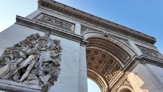 Magnificent low-angle shot moving across the detailed stone reliefs and ornate carvings of the historic arc de triomphe, a famous parisian landmark celebrating national pride and victory